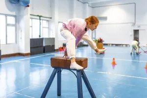 Girl practicing gymnastics, balancing on pommel horse in school gym