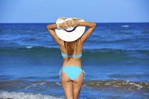 Girl young standing looking at the sea with beach hat rear back view