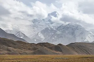 Glaciated, cloud-covered mountain peaks and golden meadows
