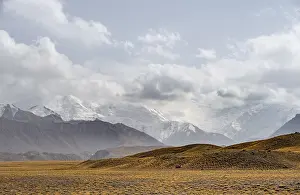 Glaciated, cloud-covered mountain peaks and golden meadows
