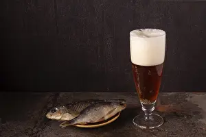 A glass of beer and dried fish on a sheet of rusty iron