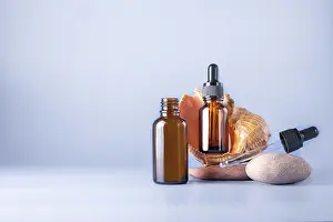 Two glass brown bottles with a pipette for a cosmetic product with a sea shell on stones