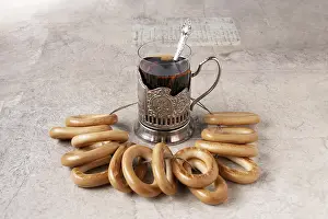 A glass of tea in a metal cup holder and a bunch of bagels on the table