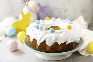 Glazed easter lemon cake decorated with confectionery and mini chocolate eggs candy on gray stone background