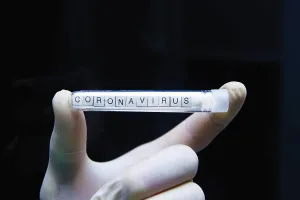 A gloved hand displays a test tube labeled coronavirus against a black background