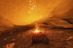 A glowing fire in a cave with a sleeping bag lying next to it creates an atmospheric scene