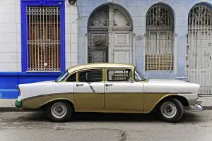A gold-white vintage car stands in front of a stylish house facade