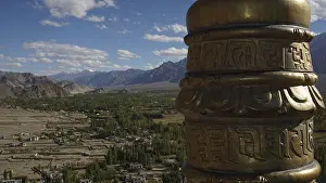 Detail of a golden prayer wheel against the backdrop of a vast mountain landscape