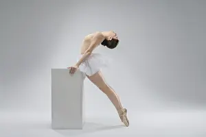 A graceful ballerina leans back elegantly while balancing on a sturdy block