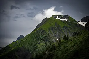 Grassy summit with remnants of snow and dramatic clouds