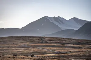 Gravel road through autumnal plateau with brown grass