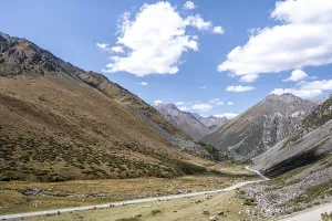 Gravel track in a valley, picturesque mountain landscape with white mountain peaks