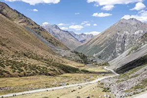 Gravel track in a valley, picturesque mountain landscape with white mountain peaks