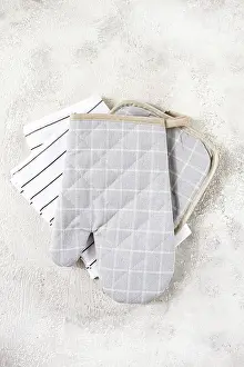 Gray checkered oven mitts and simple kitchen towels are neatly arranged on a soft