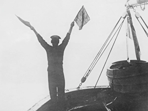 During The Great War 1914-1918. A sailor seen signalling from one British warship to another. Depending on how the two flags were positioned, the combinations meant different letters and numbers