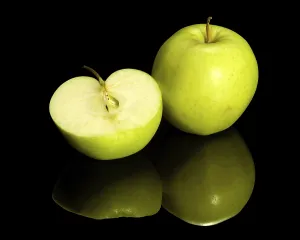 Green apple and halved on dark reflective ground