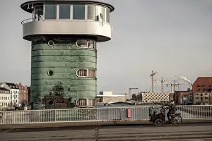 A green architectural tower by a bridge with a cyclist and cranes in the urban scene in Copenhagen