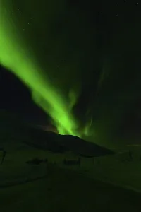 Green aurora borealis illuminating a dark landscape with hills and starry sky