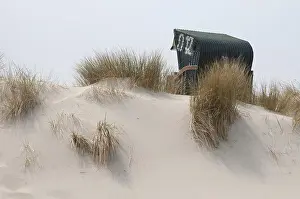 A green beach chair stands behind an area of dune grass in the sand
