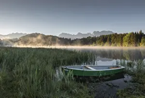 A green boat on the shore of a lake (Geroldsee) shrouded in morning mist