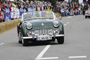 A green classic roadster drives on a road at a classic car race