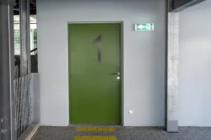 Green fire exit door number one with illuminated sign showing escape route and tactile paving