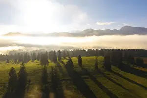 Green meadow in morning light, surrounded by fog and mountain skyline