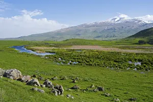Green meadows with a meandering stream and a mountain range in the background under a clear sky