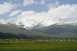 Green meadows in front of snow-covered mountains under a cloudy blue sky