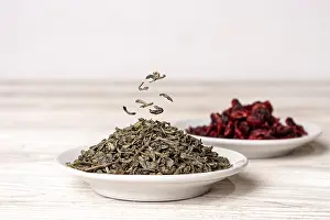 Green tea and dried cranberries lie in saucers on a white wooden background