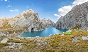 Green tent at the turquoise mountain lake Kol Suu with rocky steep mountains