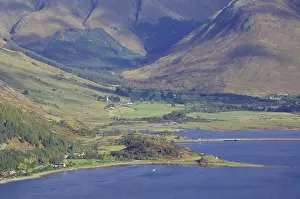 Green valley with a body of water and surrounded by high mountains under a blue sky