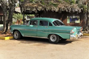 Green and white vintage car in perfect condition parked in front of a building in tropical Cuba