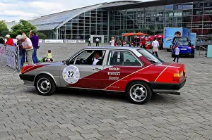 Grey-red car at a vintage car event with modern architecture in the background