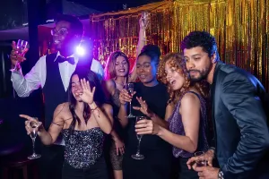Group of cheerful elegant friends having fun together and drinking sparkling wine while dancing