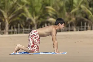 The guy of Asian appearance practices yoga on a beach against palm trees