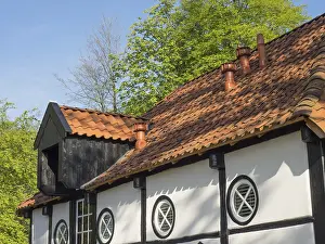 Half-timbered house with round window and tiled roof in a rural setting