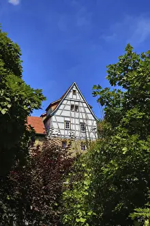 Half-timbered house towering between green trees in the blue sky