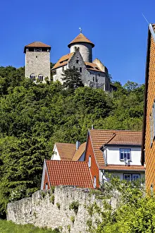 Half-timbered houses with red roofs in front of a castle on a wooded hill