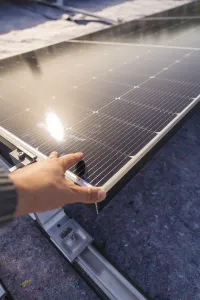 A hand adjusts a solar panel on a roof in the sunlight