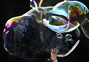 A hand bursts a large iridescent soap bubble against a black background
