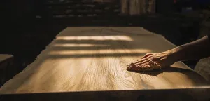 A hand gently sanding a wooden surface under warm lighting