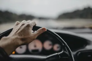 A hand gripping the steering wheel with a blurred view of the road ahead