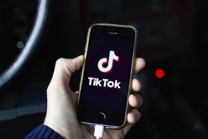 A hand holding a smartphone displaying the TikTok app on a dark background