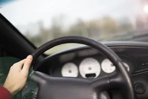Hand holding a steering wheel inside a car with dashboard in view