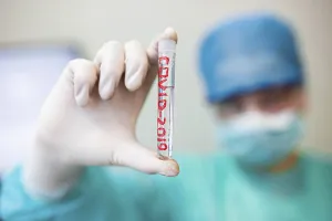 Hand holds a test tube labeled COVID-2019 against a blurred medical background