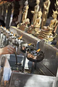 A hand pouring oil to burn in lotus-shaped metal bowls