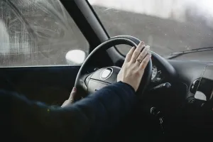 Hand resting on a steering wheel as if about to press the horn