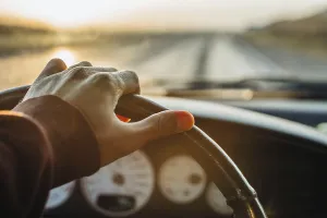 A hand on the steering wheel driving down a highway during a sunset