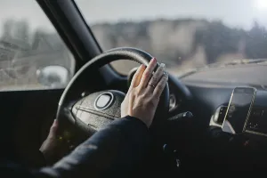 A hand on the steering wheel inside a car with a smartphone holder attached